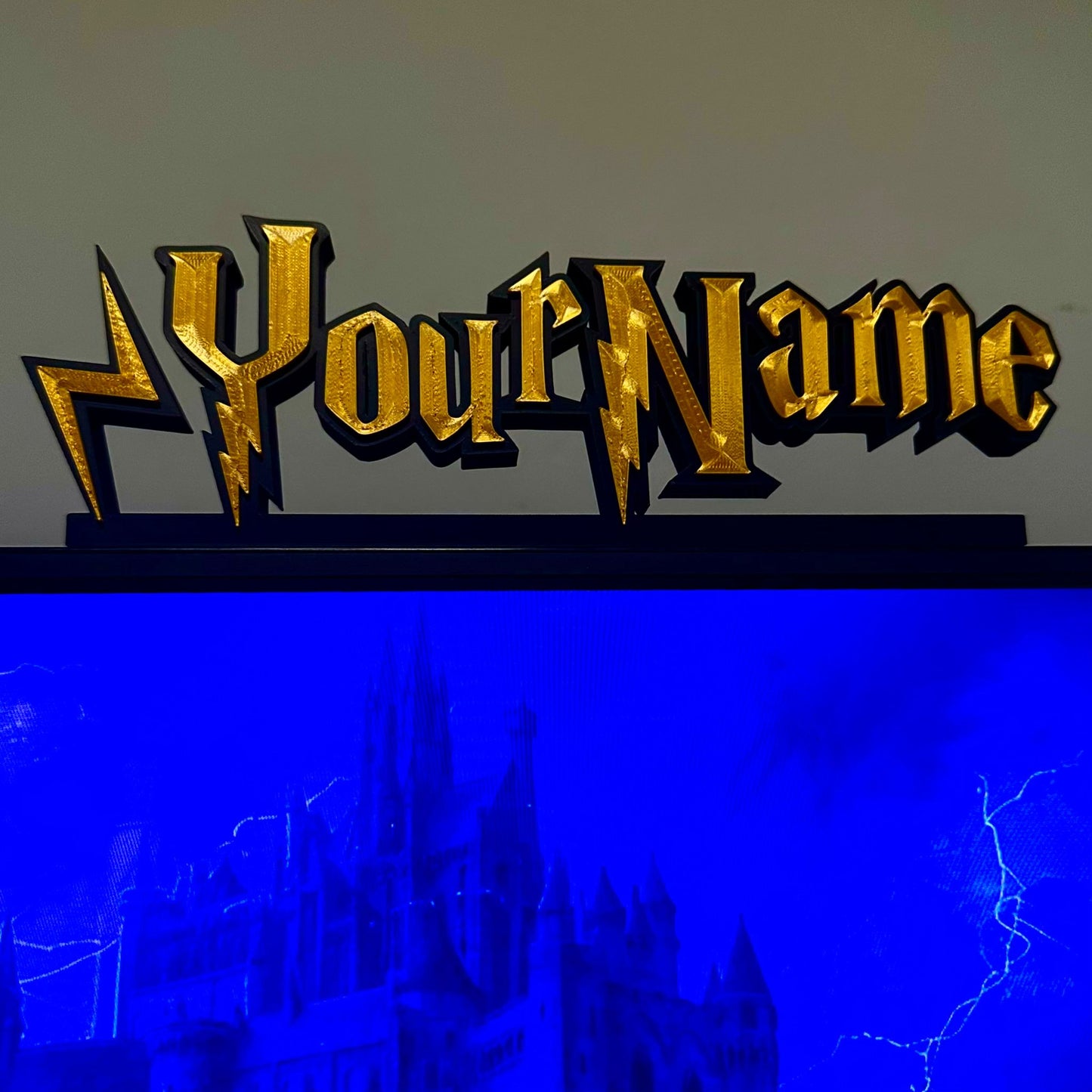 Gold 'Your Name' nameplate with lightning bolt design on a black stand against a blue and gray background.
