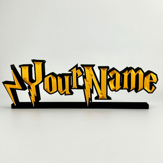 A custom made nameplate in a wizard style font. Gold 3d text on matte black background, freestands upright on a black base.