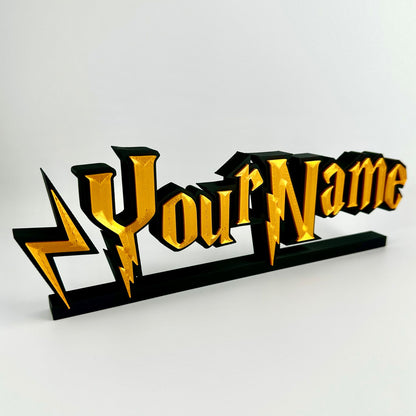 A custom made nameplate in a wizard style font. Gold 3d text on matte black background, freestands upright on a black base.