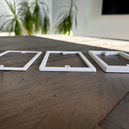 Three rectangular plastic spacer plates for light switches or sockets, laid out on a wooden surface. They are white in colour and each have a different thickness, showing that they are custom made for different requirements.