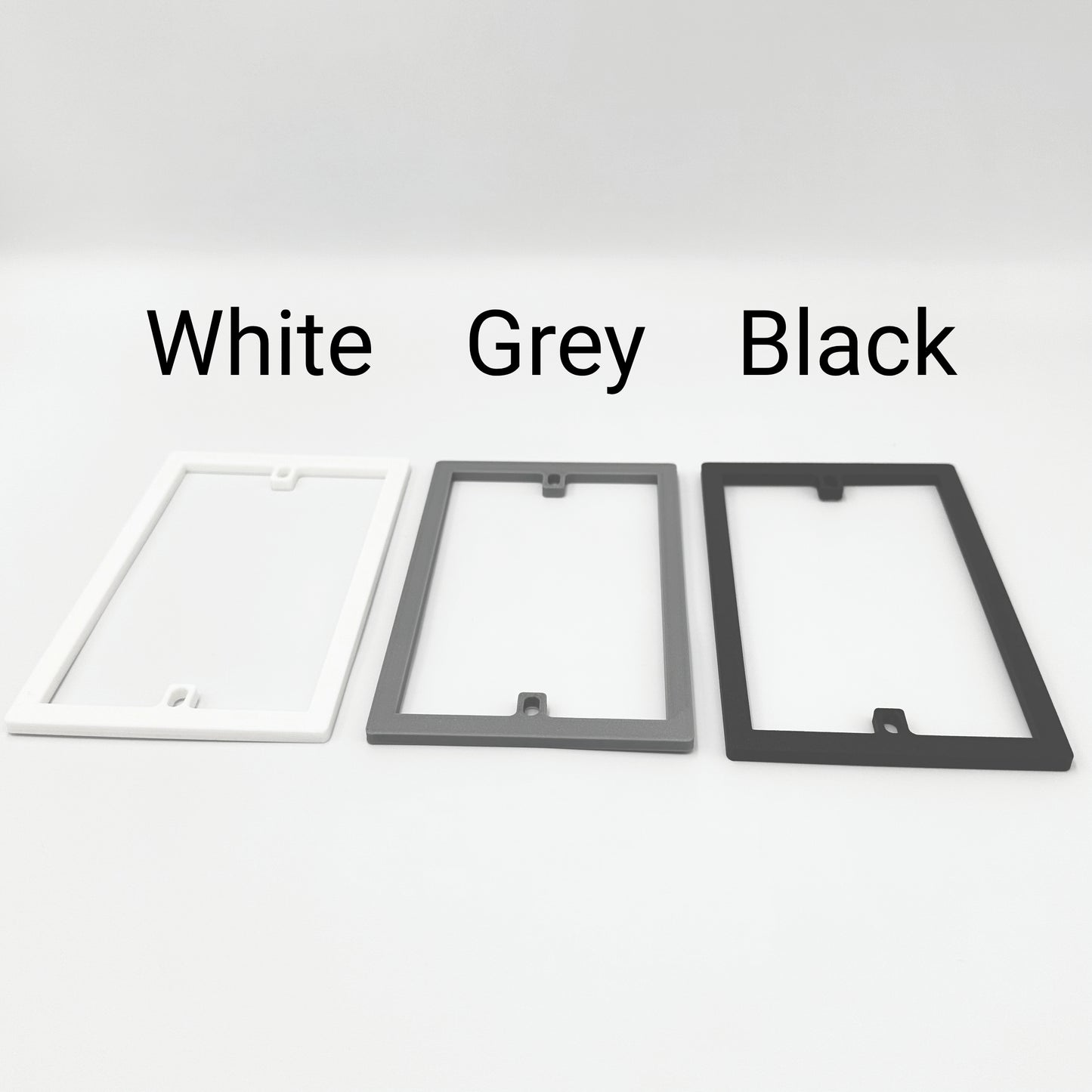 Three rectangular socket spacer / extension frames in white, gray, and black with labels above each to show the different colours available.