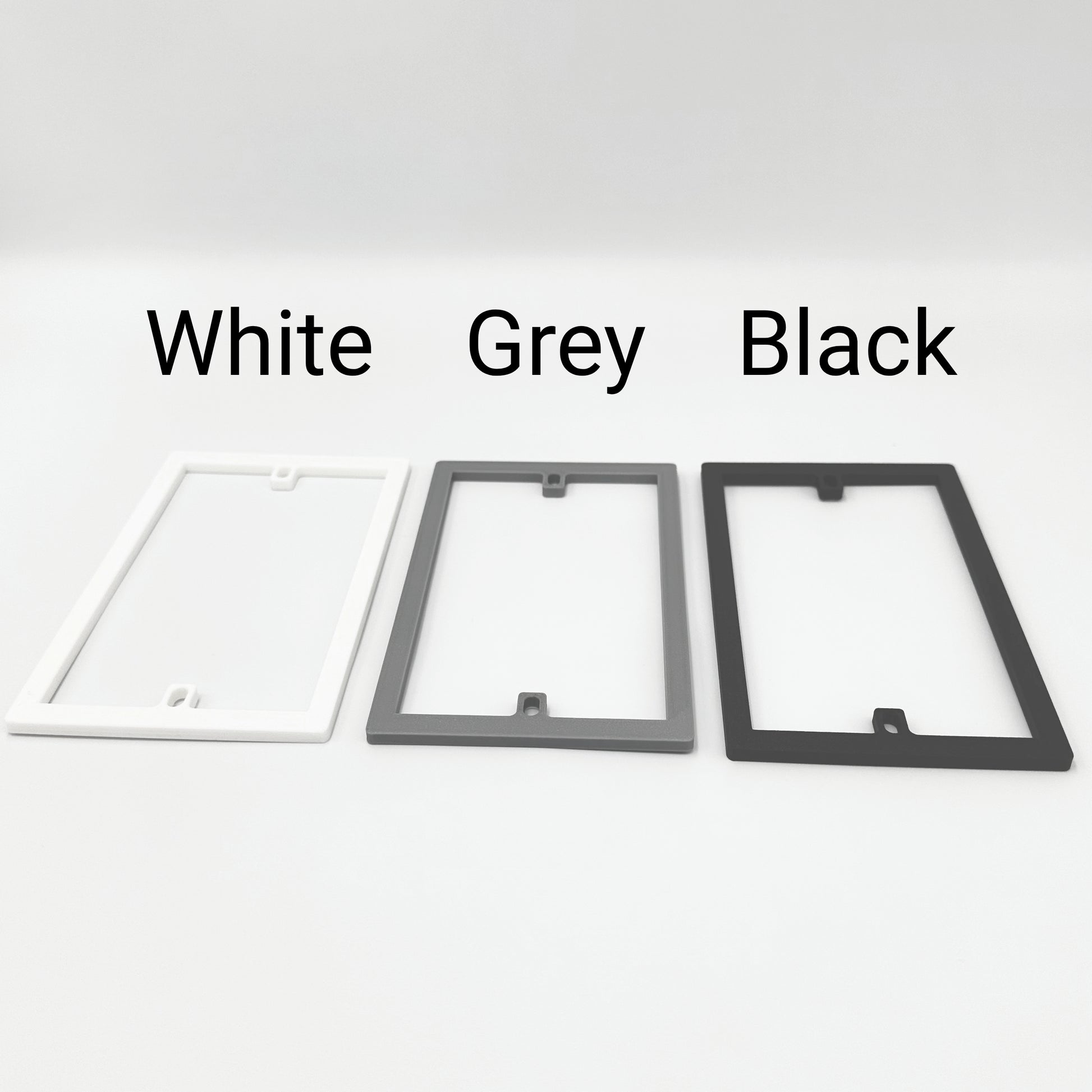 Three rectangular socket spacer / extension frames in white, gray, and black with labels above each to show the different colours available.